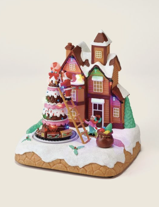 A festive gingerbread house scene featuring a decorated Christmas tree with lights, a ladder, and colorful candy decorations on a snowy base.