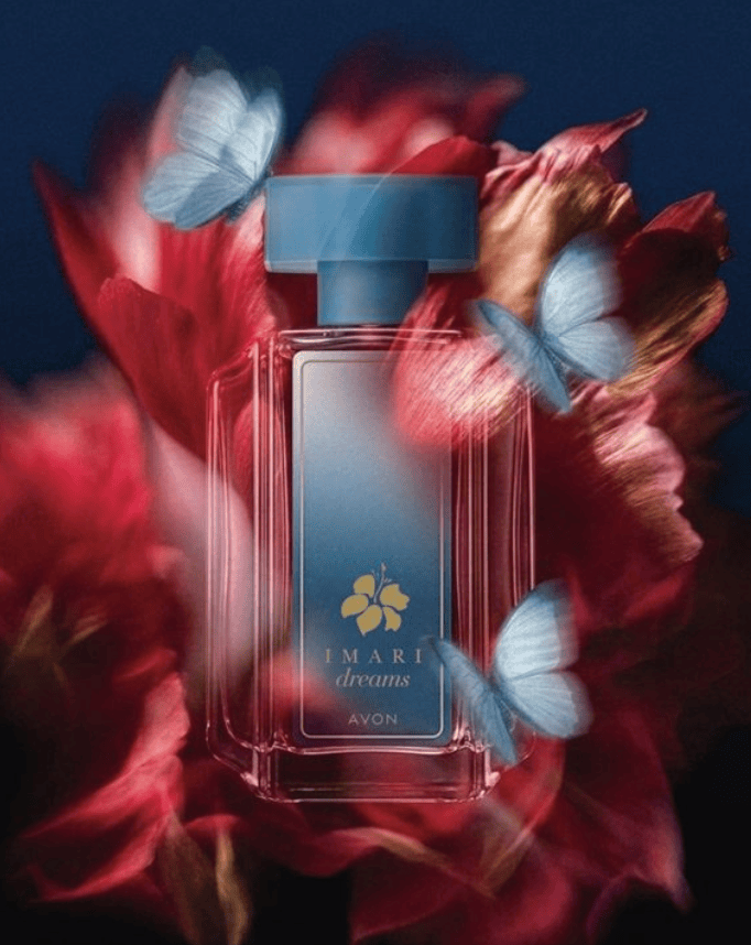 A bottle of Avon perfume named 'Imari Dreams' set against a blurred floral background, with delicate blue butterflies surrounding it.